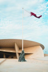Stunning view of the National Museum of Qatar with the Qatari flag waving against a blue sky.
