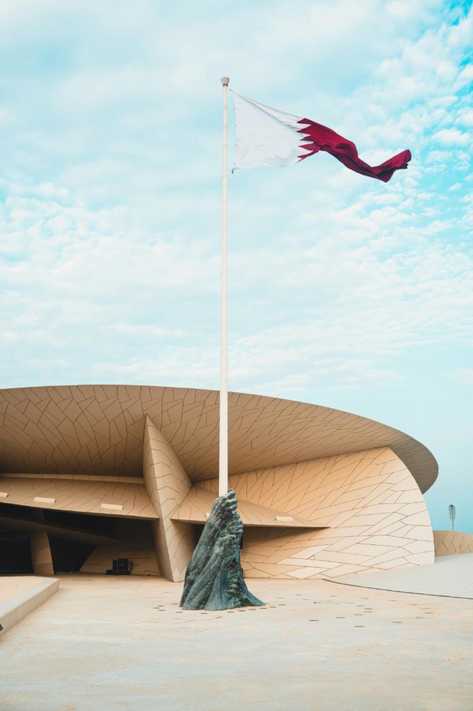 Stunning view of the National Museum of Qatar with the Qatari flag waving against a blue sky.