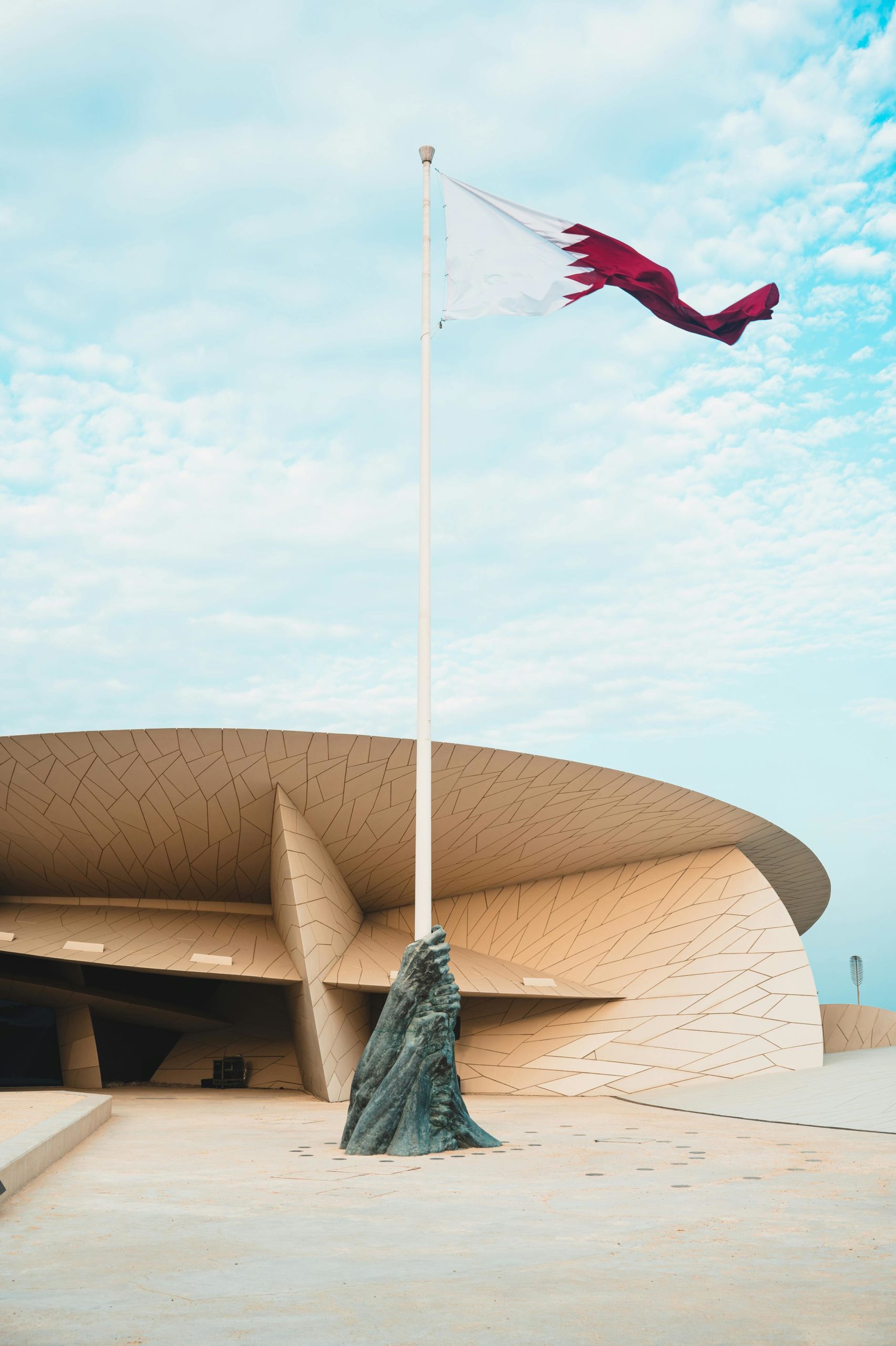 Stunning view of the National Museum of Qatar with the Qatari flag waving against a blue sky.